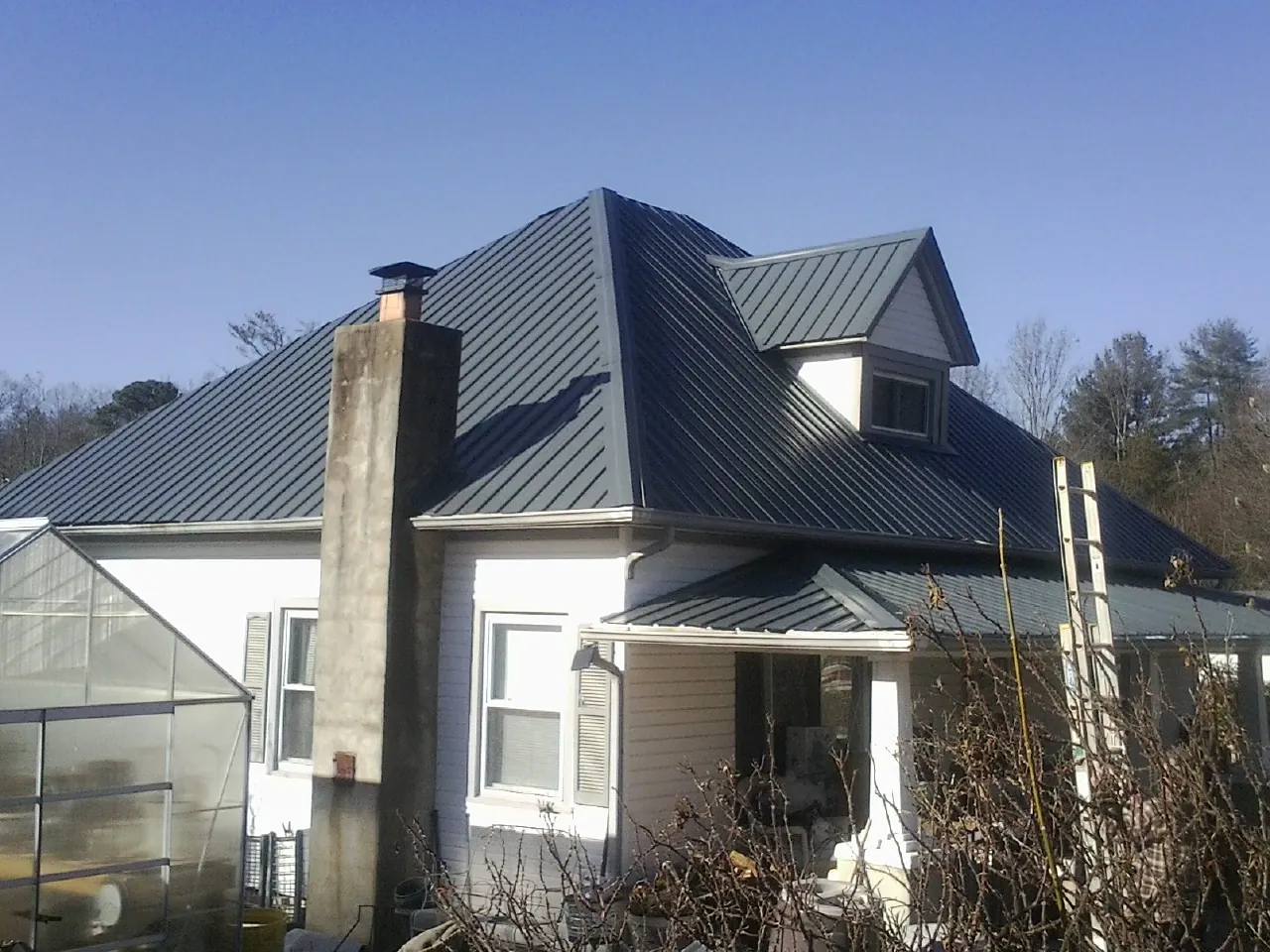 Dark blue standing seam metal roof on a white farmhouse with dormer — Slate & Tile Roof Repair by Roofing Brothers in Lovelock