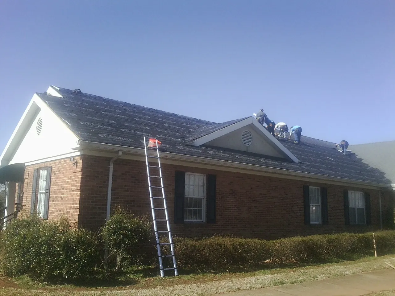 Crew tearing shingles off a brick ranch roof with a ladder set — Emergency Roof Repair work by our crew in Lovelock