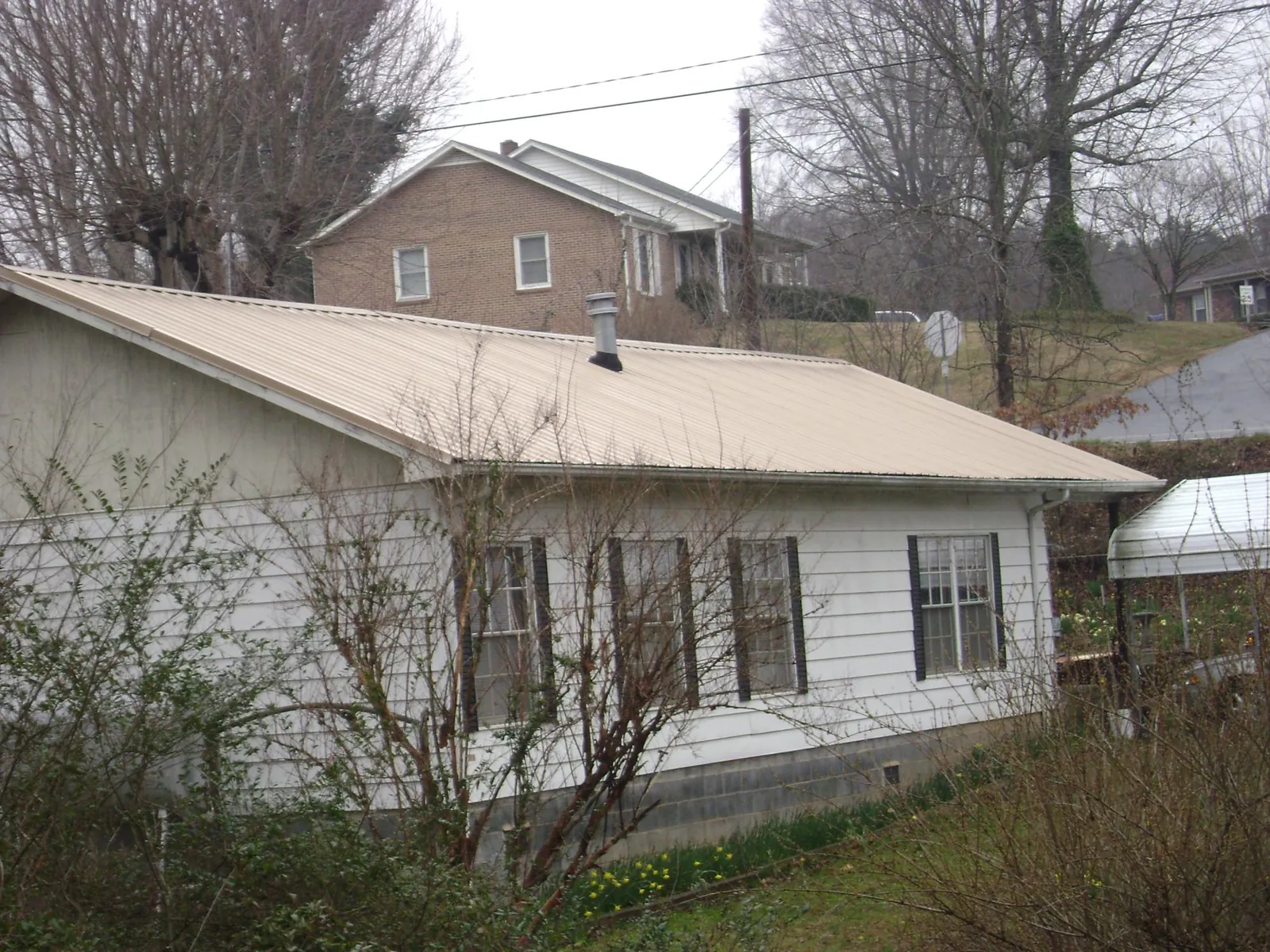 Tan metal roof on a white sided house set into a hillside — Commercial Roofing by Roofing Brothers in Lovelock